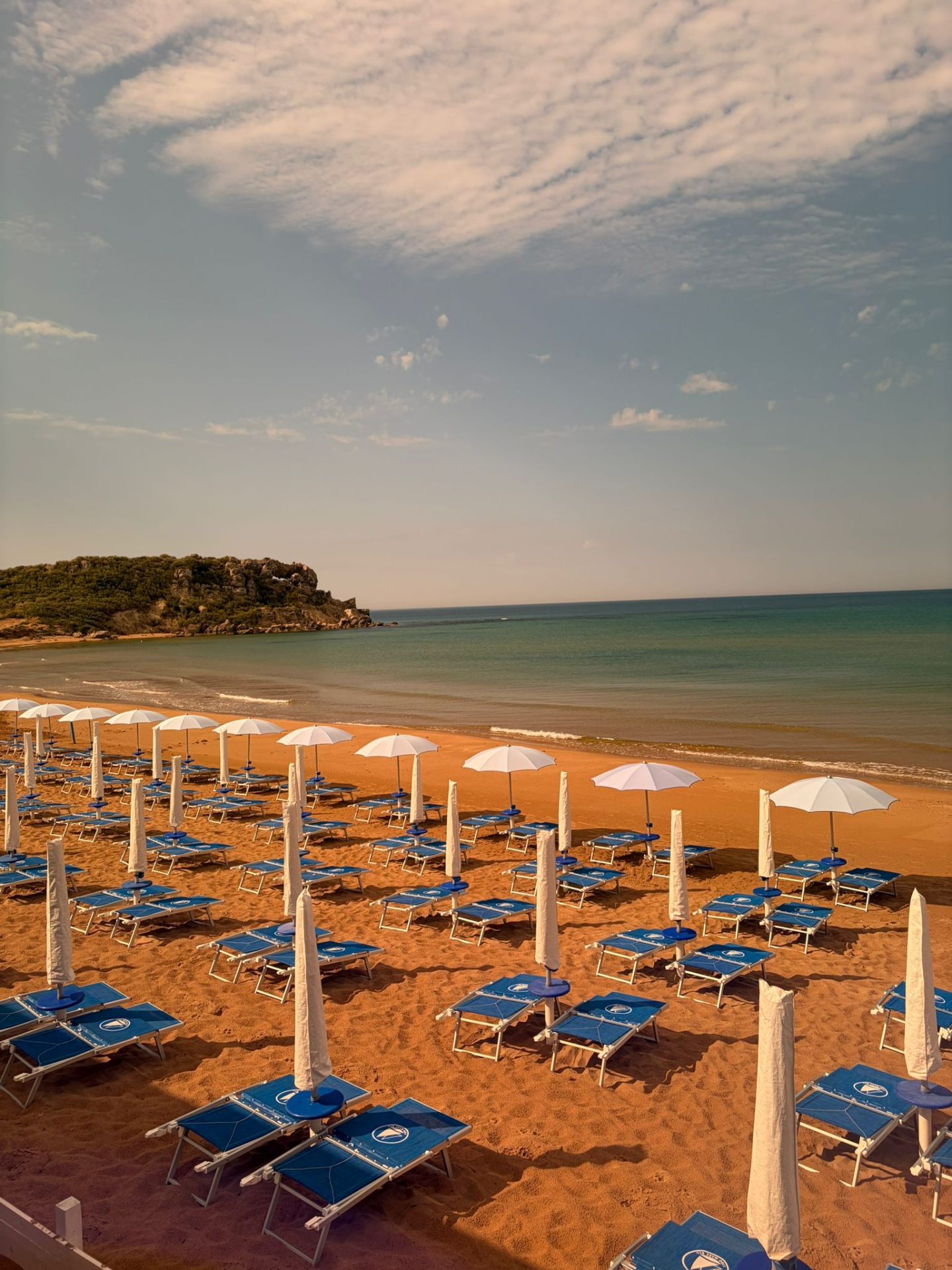 Baia con file di ombrelloni bianchi e lettini blu sulla sabbia dorata