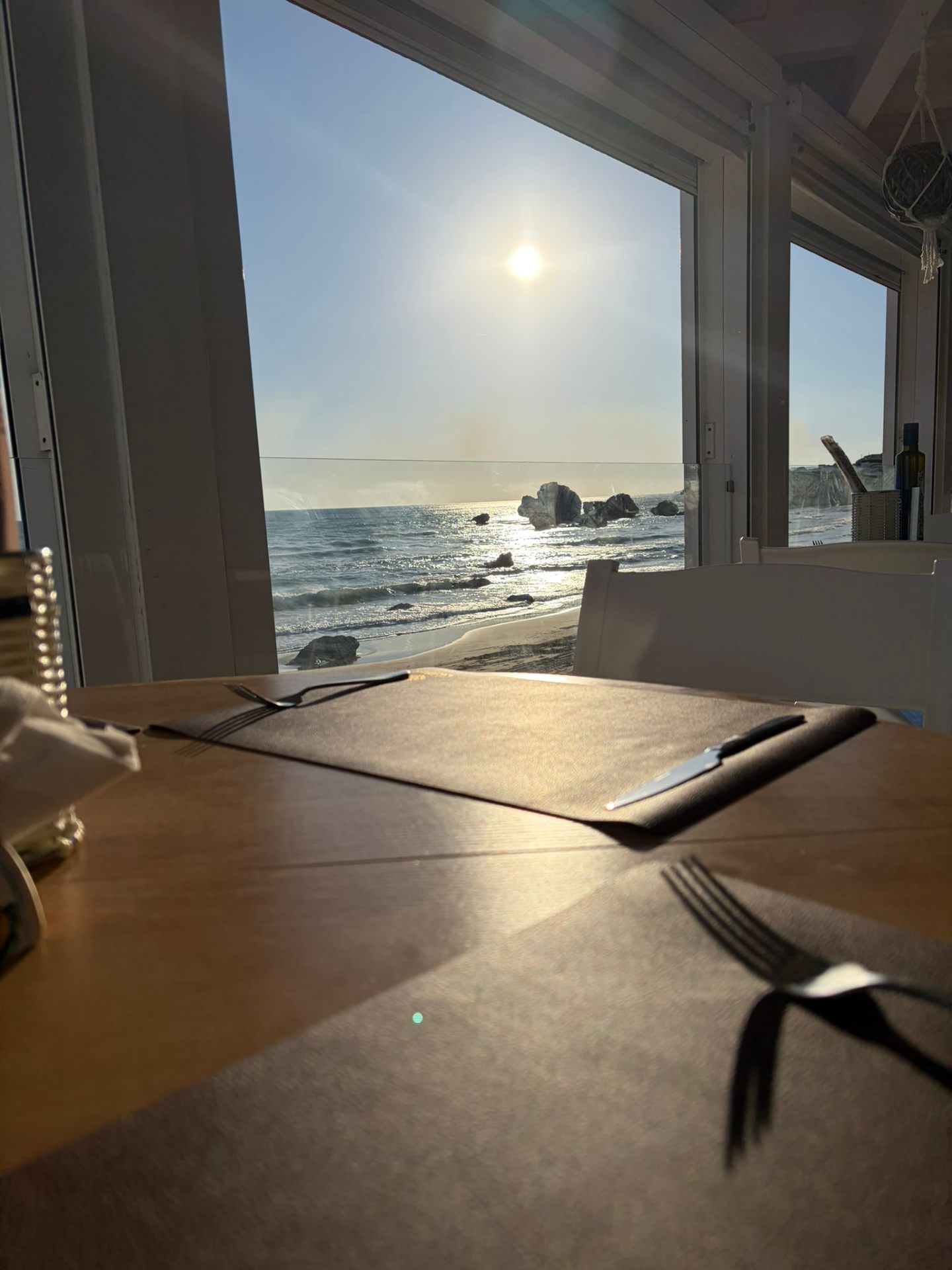 Tavolo apparecchiato con vista sul mare, sole e scogli
